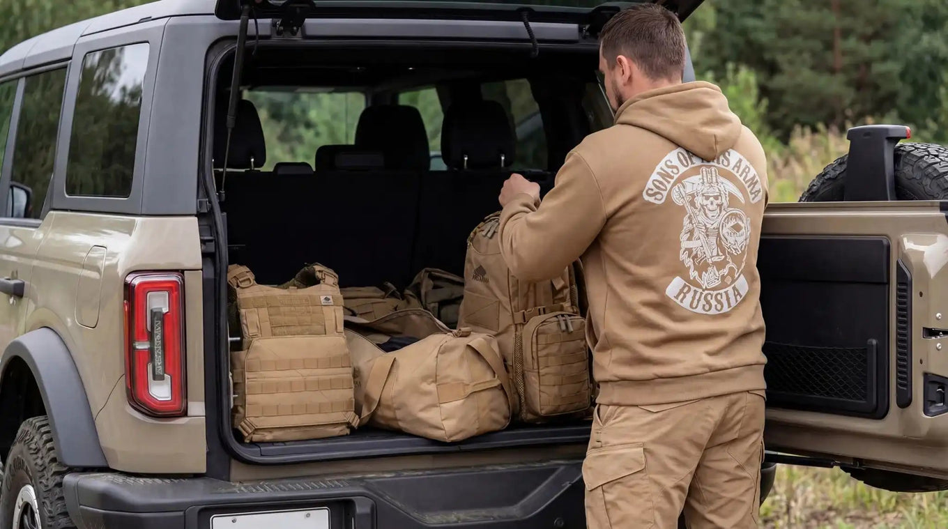 Man in an A-26 Azimuth hoodie loads things into a car outdoors